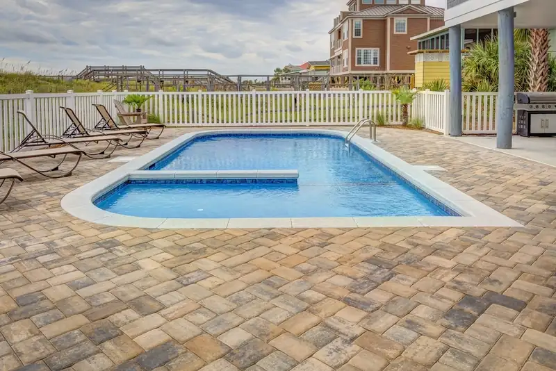 Backyard pool surrounded by a paved patio with lounge chairs